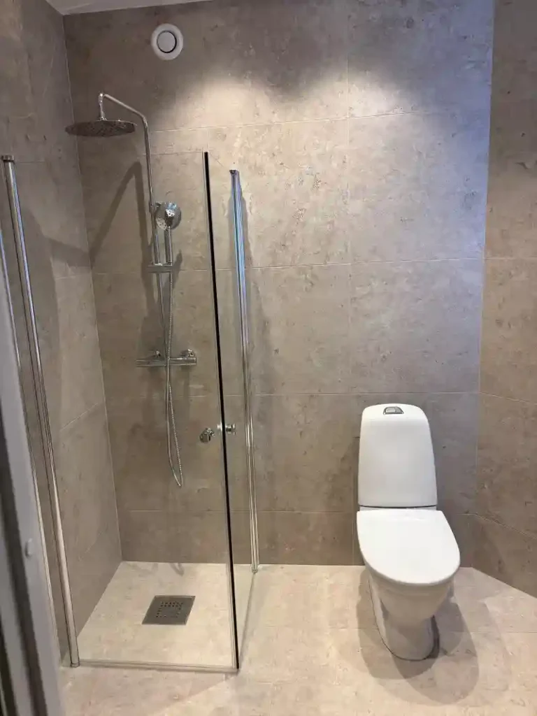 Färdig badrumsrenovering på Valhallavägen i Stockholm med glasdusch, takdusch och WC.