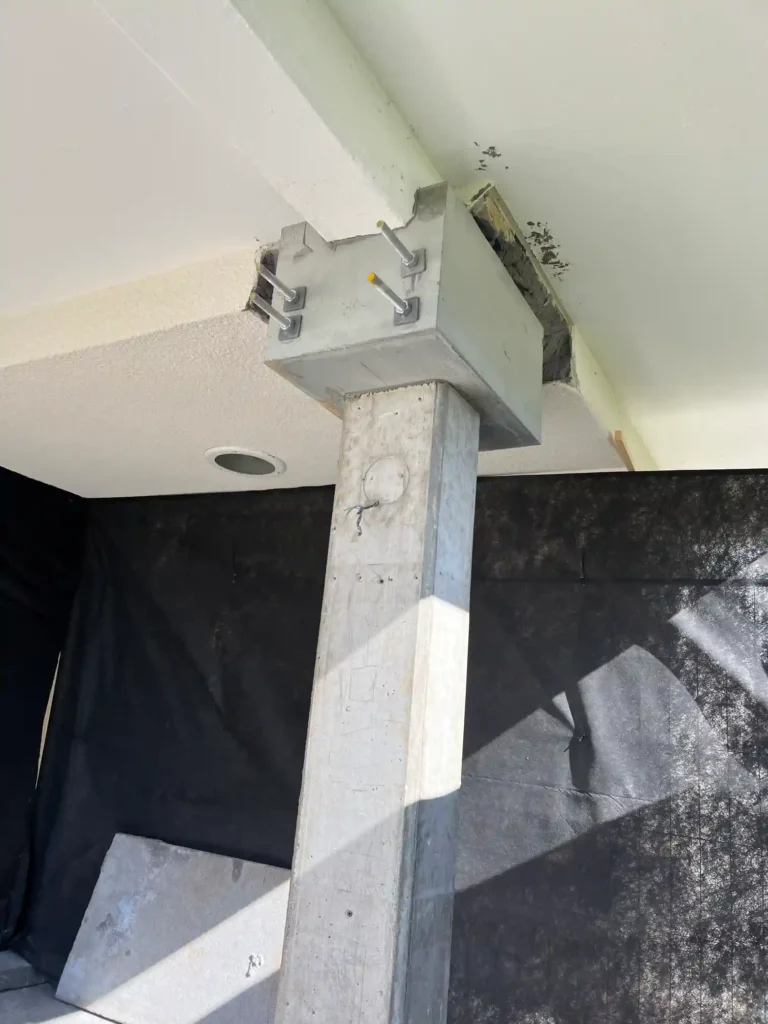 Övre delen av en betongpelare och dess anslutning till bjälklaget, med synliga metallbeslag.
