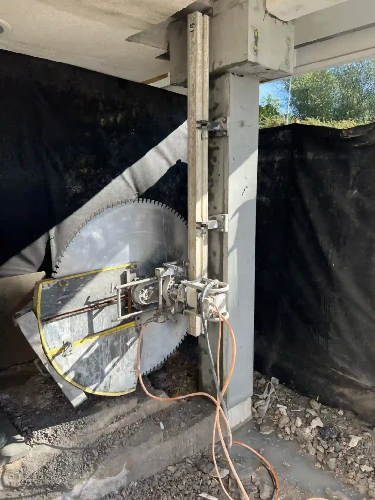 Betongsåg med stor sågklinga monterad på en vertikal skena vid en betongpelare.
