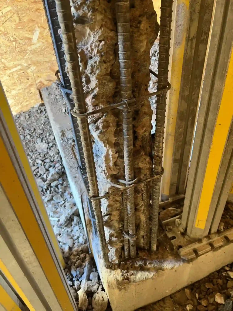 Närbild på vertikala armeringsjärn och byglar i en delvis frilagd betongpelare.