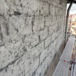 Fasad med bortknackad puts och synligt underlag intill byggställningen på Steningevägen 4 i Årsta i Stockholm.