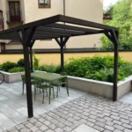 Svart pergola med bord och stolar på en stenlagd innergård hos BRF Kastanjen på Södermalm efter innergårdsrenovering.