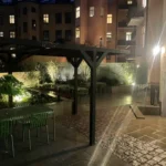 BRF Kastanjens innergård på Södermalm på kvällen, med pergola, sittplatser och belysta gångytor.