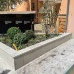 Upphöjd plantering med buskar och träd, omgiven av en låg mur och markplattor hos BRF Kastanjen på Södermalm i Stockholm.