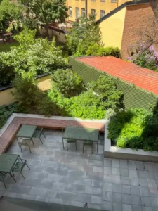 Stenlagd sittplats med träbänk, bord och stolar intill planteringar på BRF Kastanjens innergård på Södermalm i Stockholm.
