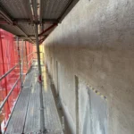 Nyputsad fasad med täckta fönster intill byggställningen på Steningevägen 4 i Årsta.